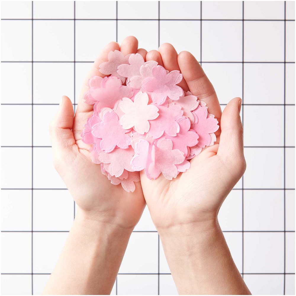 400167_AW_4 Papierblüten, rosa und pink, in Händen gehalten, Hintergrund mit weißem Gittermuster.