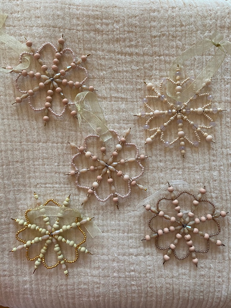 IMG_0146 Perlen-Schmuckanhänger, Schneeflockenform, Pastellfarben, Perlen und Draht, Schleifenband, fünf Stück, rosa, beige, gold, auf weißer Oberfläche.