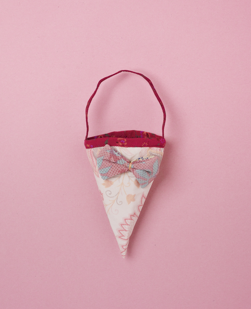 Cornet-SILK-Cornet-Pale Papiertüte in Kegelform, pastellfarbenes Muster, rosa und beige, rote Schleife vorne, roter Henkel.