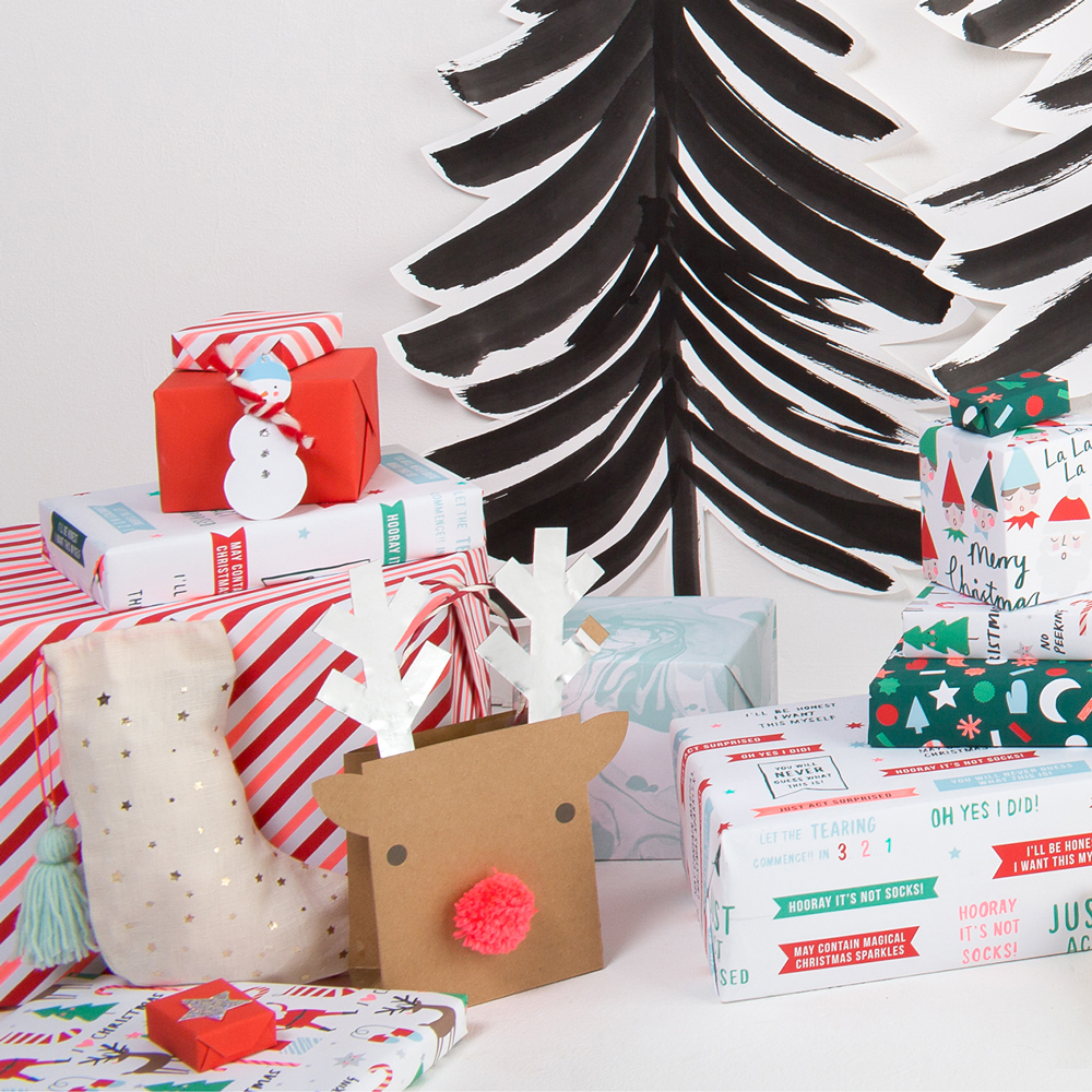 44-0149z Geschenkverpackungen, verschiedene Muster und Farben, rotes Paket mit Schneemannaufdruck, braune Geschenktüte mit Rentiermotiv, schwarze und weiße Rückenwand in Form eines Tannenbaums, gestreifte und weihnachtliche Motive.