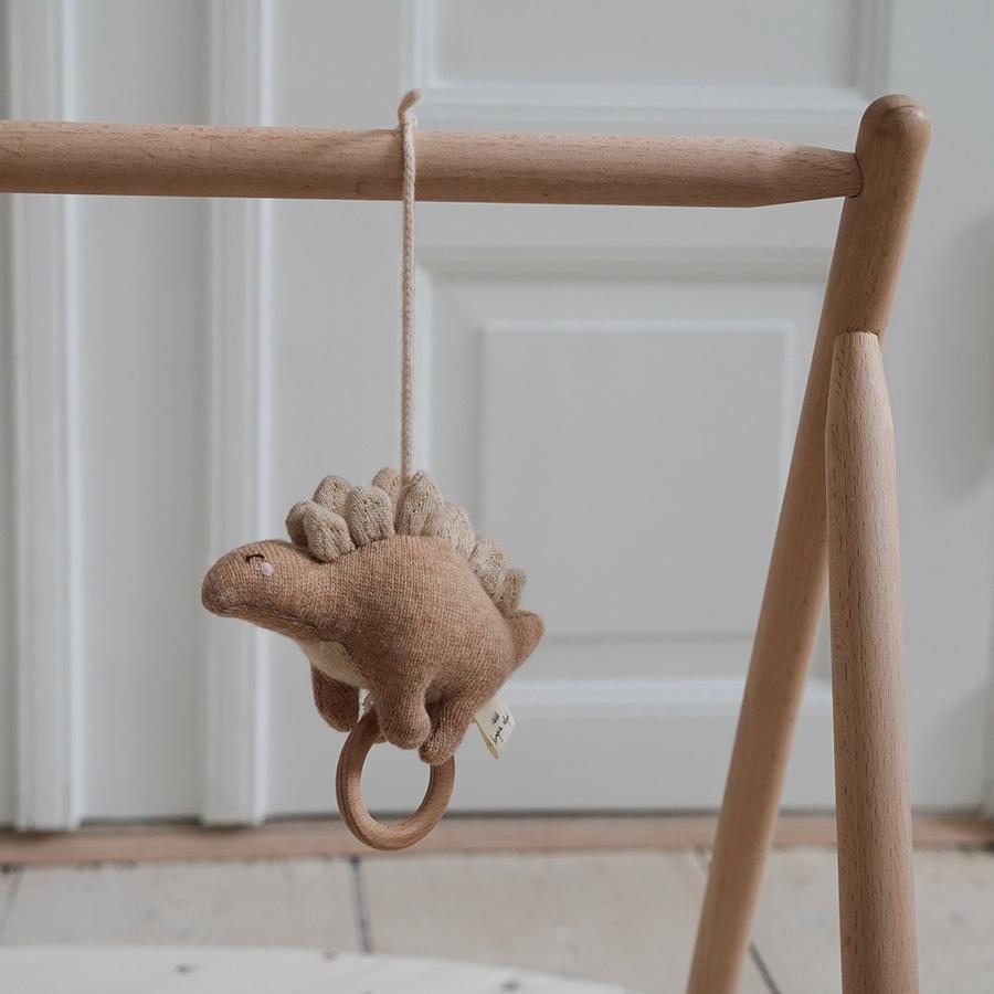 konges-slojd-spieluhr-stegosaurus-rose-3 Stofftier Dino, Braun, hängend an Holzgestell, mit Holzring, Spielzeug zur Befestigung, neutrale Farben.