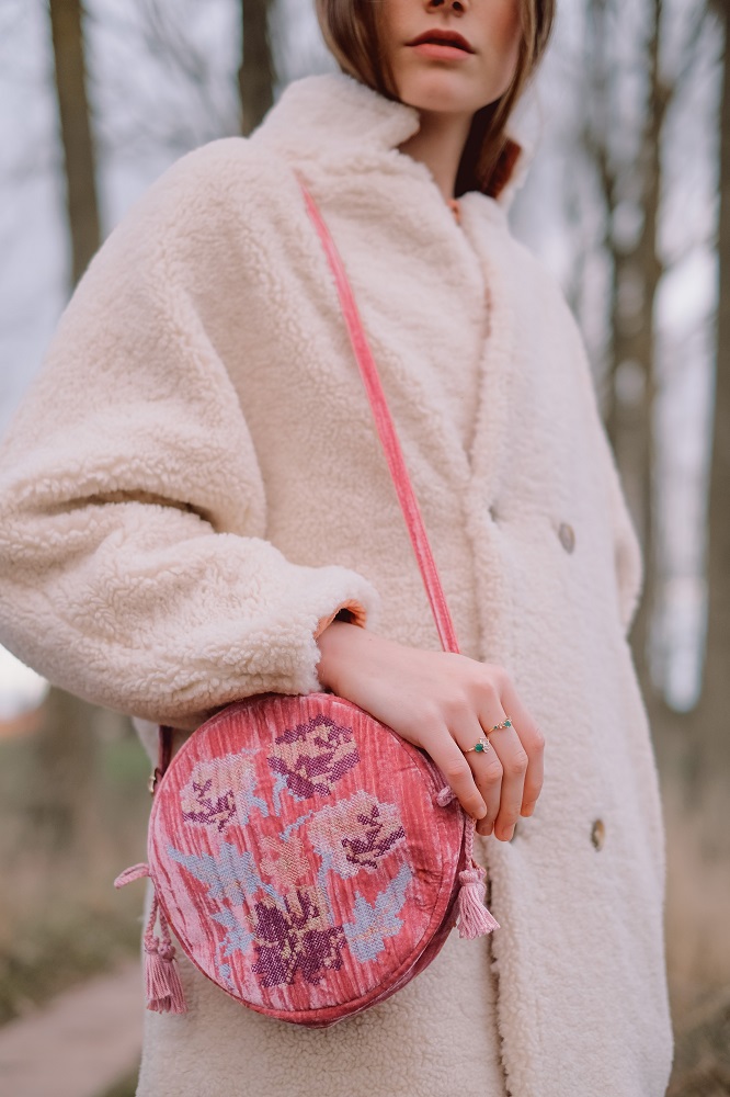 womenbagsiarusty2 Runde Handtasche, rosa, florales Muster, Quasten, Träger ebenfalls rosa, Frau im cremefarbenen Mantel.