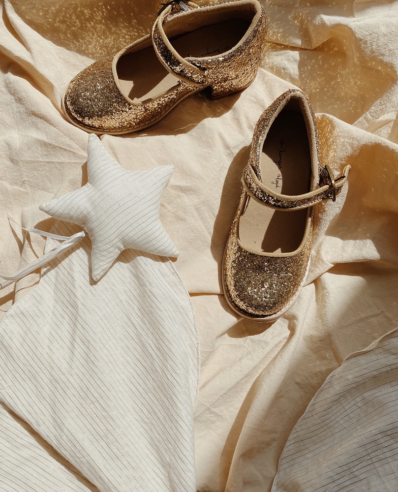 KS1933-MULTI-Main Goldene Glitzerschuhe, Mary Jane Stil, Schnallenverschluss, auf cremefarbenem Untergrund. Quilted Kissen in Sternform, cremefarben mit Streifen.