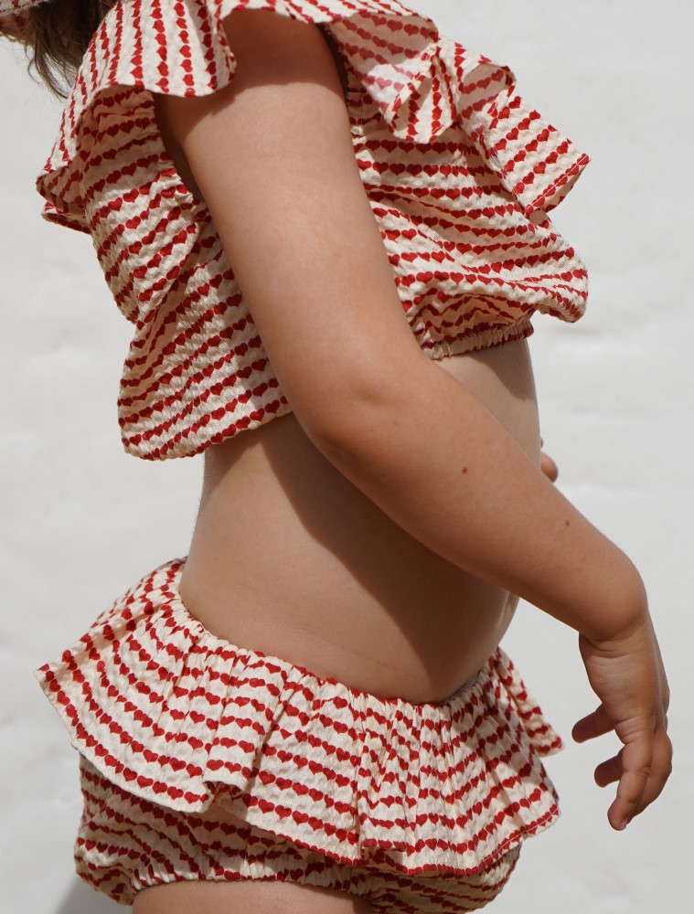 KS5263-MILLI-SUMMER-SET-HEART-ON-A-STRING-Extra-2 Zweiteiliges Kinder-Badeoutfit, rot-weiß gestreift, Herzmuster, Rüschenverzierung an Top und Hose.