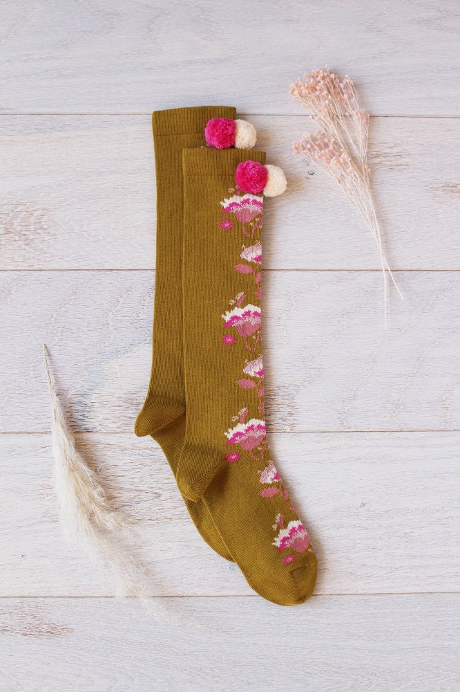 kidssocksmayumihoney1 Kniestrümpfe; olivgrün; Blumenmuster in Rosa, Weiß; Pompons in Pink, Beige; flacher Hintergrund.