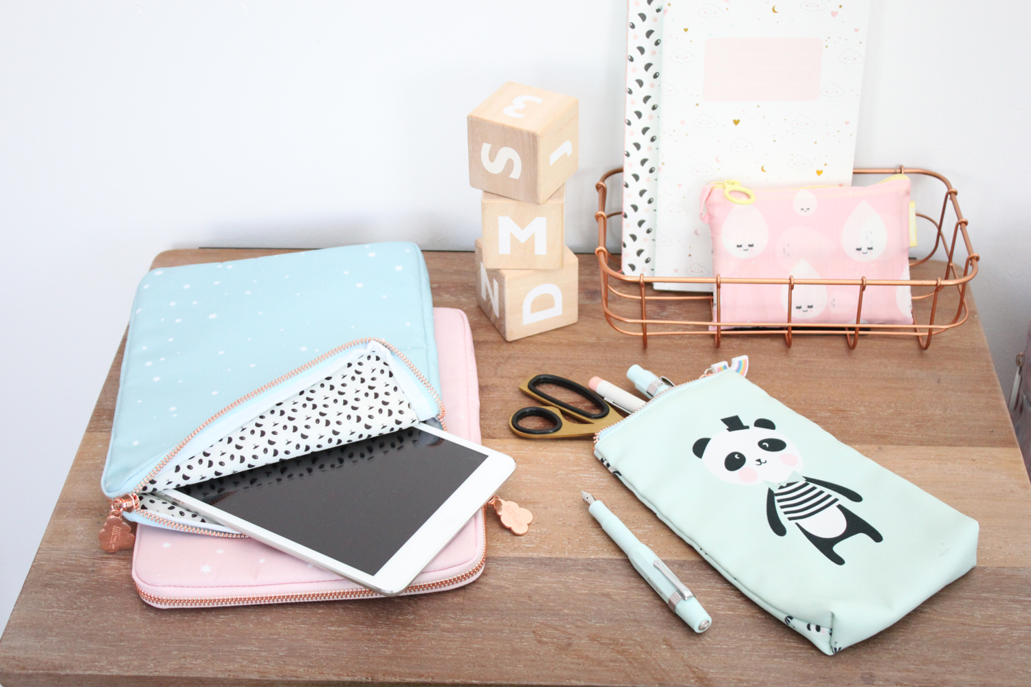 IMG_5166 Tablet-Hülle blau mit kleinen weißen Sternen, Innenfutter schwarz-weiß gemustert; rosa Hülle; mintgrünes Stiftemäppchen mit Panda-Aufdruck; Notizbuch mit Wolken- und Mondmotiven, rosa Mäppchen mit Gesichtern; Holzbuchstabenwürfel; Schere, Stifte.