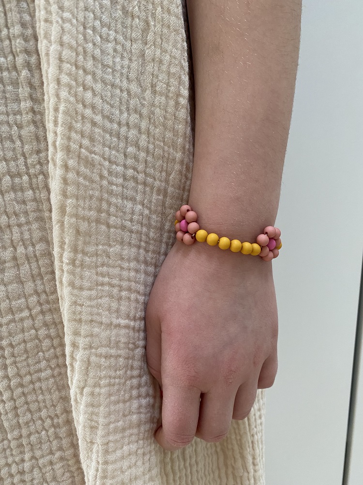 IMG_4917 Armband, Perlen, rosa und gelb, getragen am Handgelenk, beiges Kleid im Hintergrund.