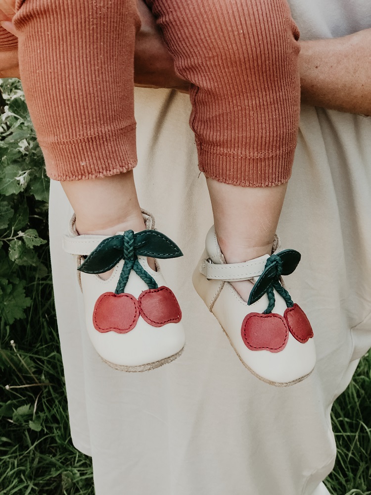 IMG_4877-2 Babyschuhe, cremefarben, Kirschen-Aufdruck, Klettverschluss, dunkle Blätter, rote Hose.