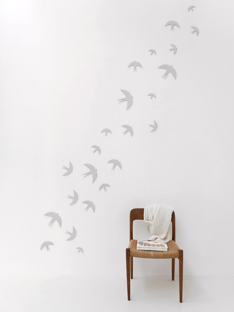 sverm-birds-large Wanddekoration, graue Vogelsilhouetten, fliegende Anordnung, minimalistisch, weiße Wand, Holzstuhl, beige Decke.