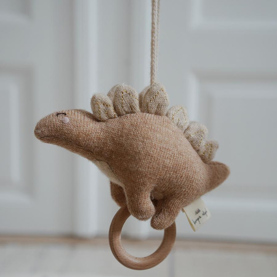 konges-slojd-spieluhr-stegosaurus-rose-2 Braunes Plüsch-Dinosaurier-Spielzeug, Stoff aus Strick, beige Rückenplatten, Holzring unten, Aufhängung an der Oberseite.