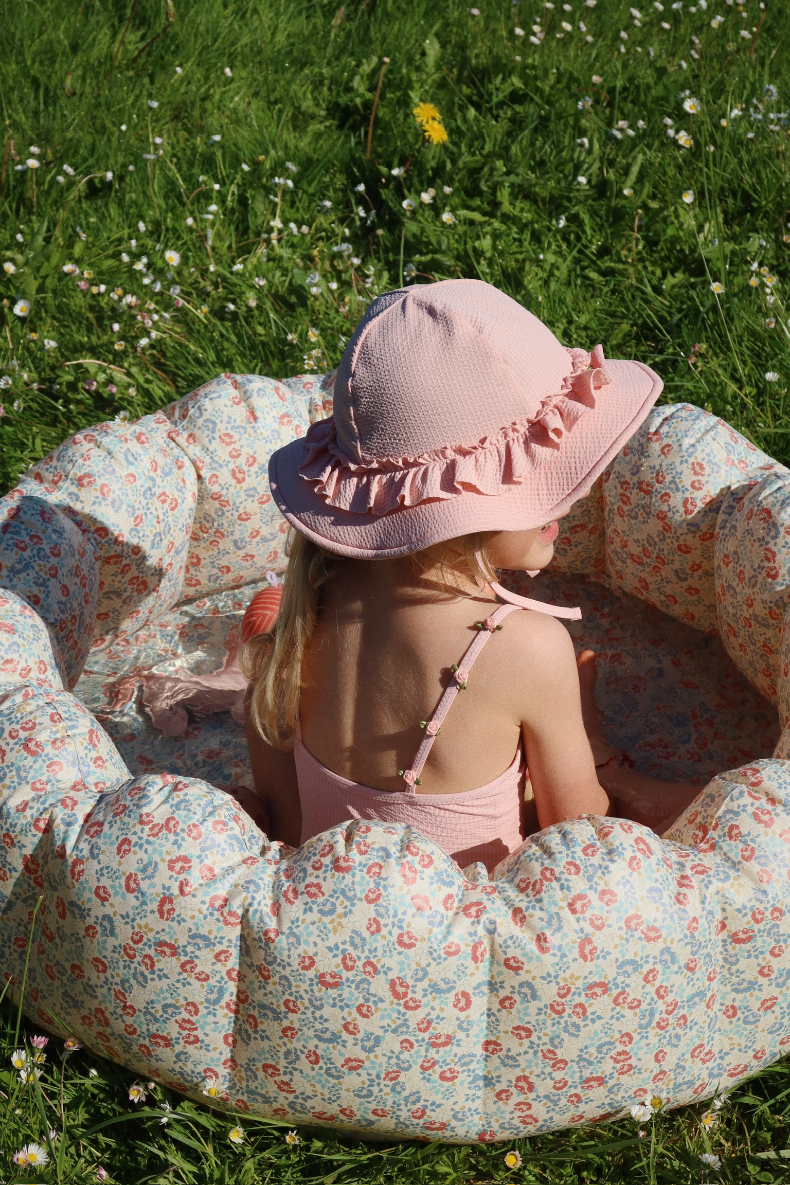 Aufblasbares Kinderplanschbecken, Blumenmuster, Kind mit rosa Sonnenhut und Badeanzug, Outdoor.