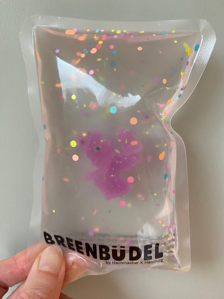 IMG_9233 Transparentes Beutelspielzeug mit pinkem Bärenmotiv, bunte Konfetti-Elemente, Aufdruck „Breenbüdel“ unten.