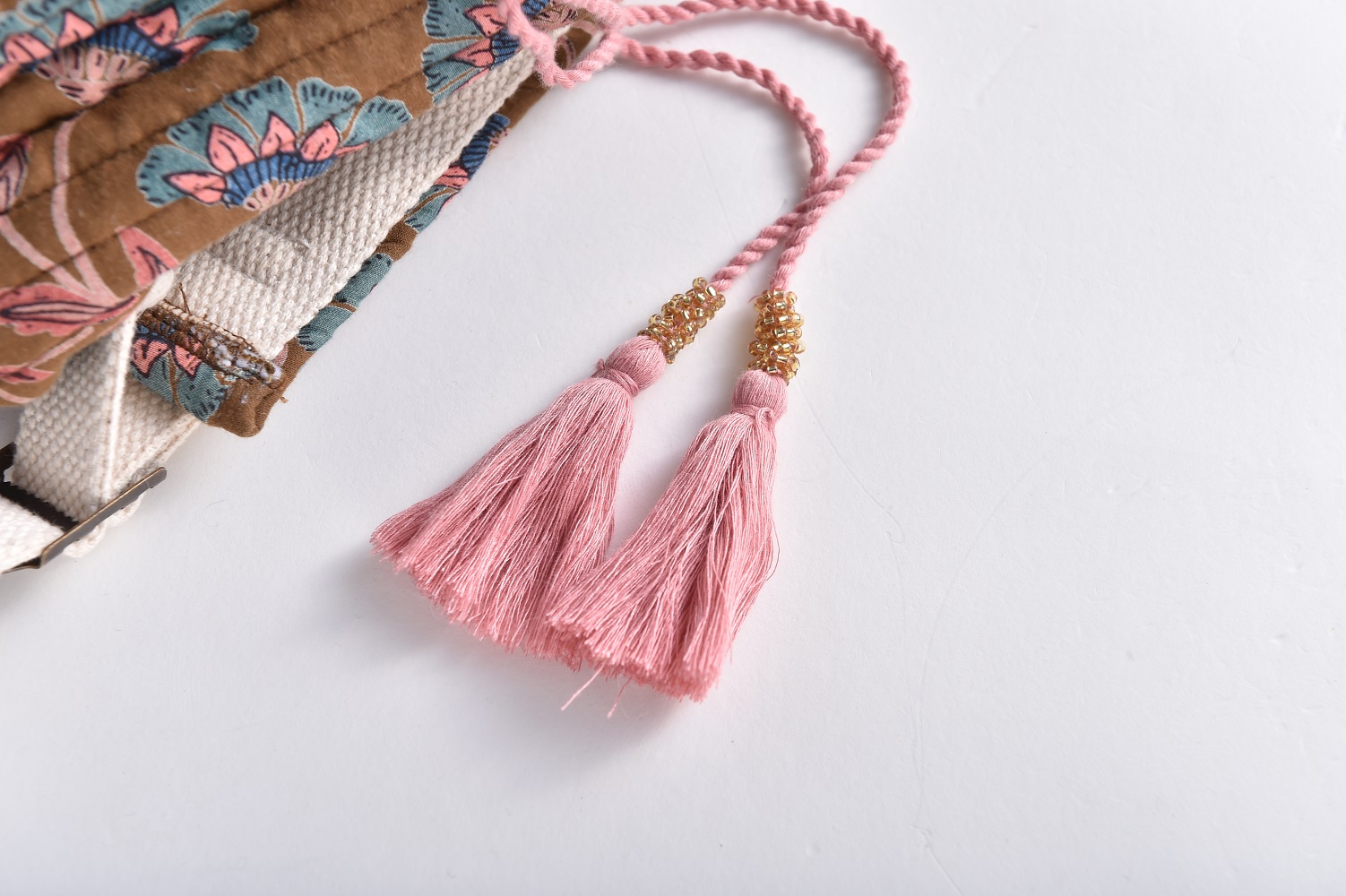 Girls-Backpack-Arti-BronzeFolkFlowers-10 Brauner Baumwollstoff mit floralem Muster, naturweißes Band, rosa Quasten mit goldfarbenen Perlenabschlüssen.