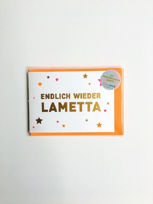 7a75ef_e123391c49de433d800d37ed8685cfab_mv2 Karte, weiße Vorderseite, goldener Aufdruck "Endlich wieder Lametta", umgeben von bunten Sternen, orangefarbener Hintergrund, runder Aufkleber "mit handbemalter Kante".