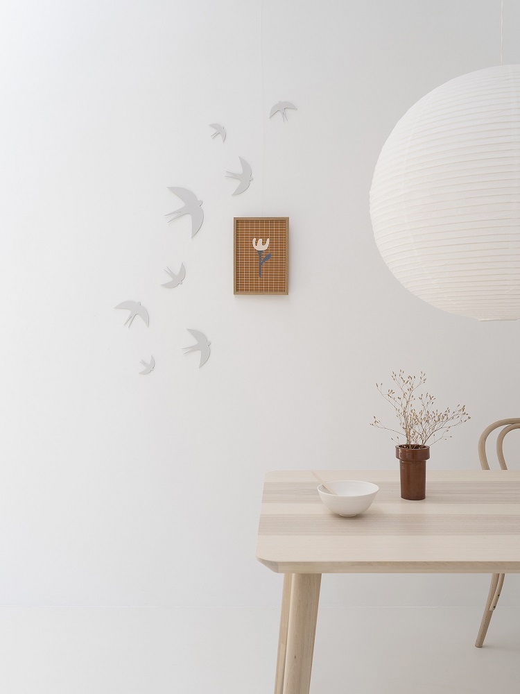 sverm-birds-small Holztisch, weiße Schale, braune Vase mit Zweigen, weiße Wandsilhouette von Vögeln, quadratisches Bild mit Tulpenmotiv, große Papierlampe.
