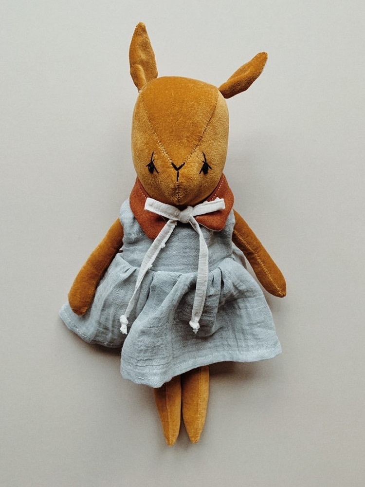47FB55F0-DC54-4DDD-9D7F-207A054AE9D2-002 Stofftier Hase, braun, Kleid grau-weiß mit weißen Bändern, Schleife am Hals, Ohren spitz, Gesicht schlicht genäht.